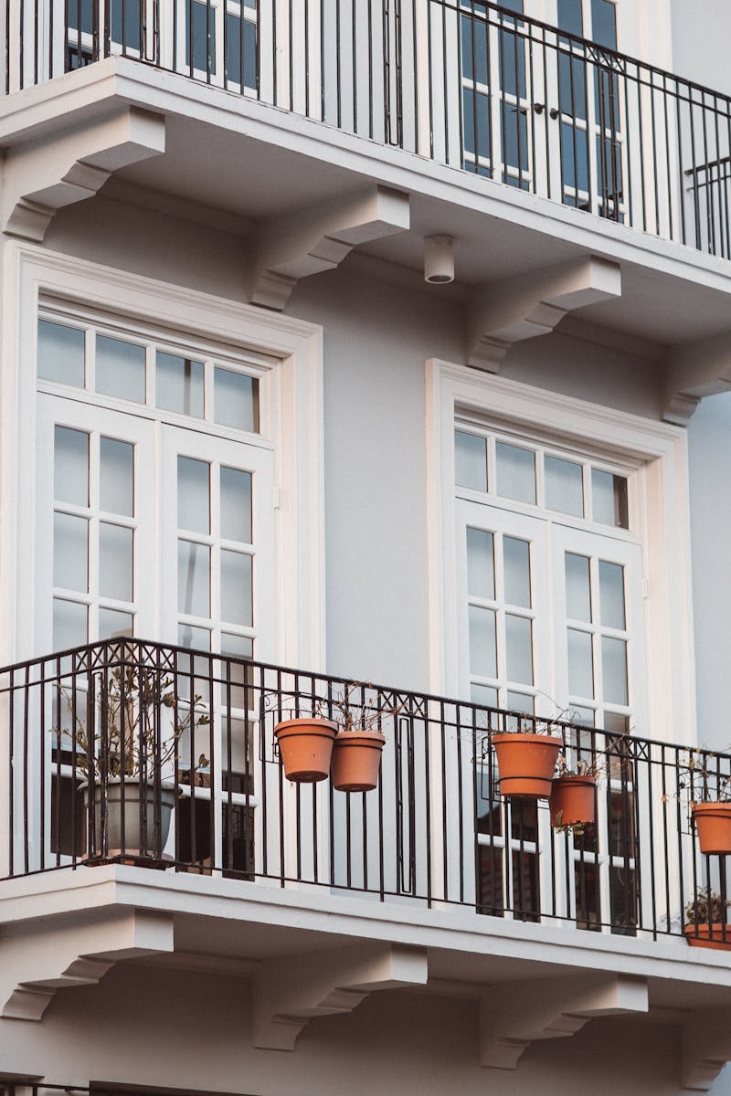 Front view of a modern building with balconies, pots, and white framed windows.